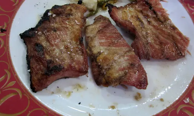 Tres trozos de lomo adobado a la parrilla, jugosos y con sal gruesa, servidos en un plato blanco con borde rojo.