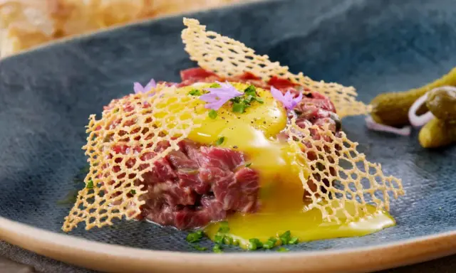 Delicioso steak tartar con huevo crudo, crujiente de queso y pepinillos. Una receta para disfrutar.