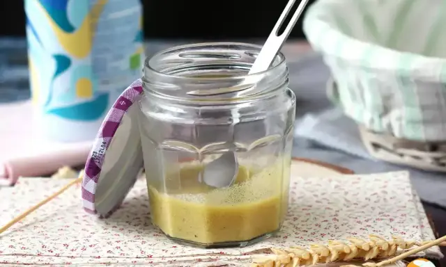 Un bocal de vinaigrette maison, prêt à assaisonner une salade fraîche. Une cuillère repose dans le mélange jaune pâle.