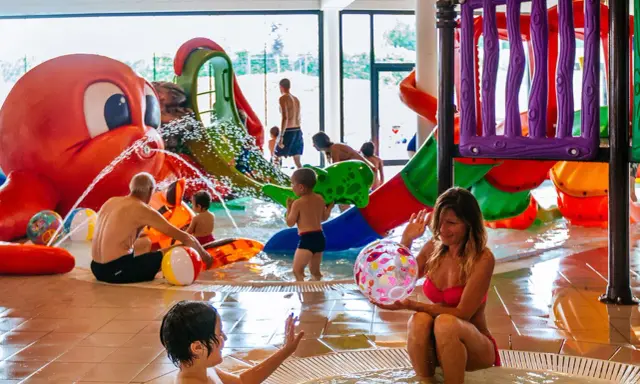 Bambini e adulti si divertono nelle **terme per bambini** con scivoli colorati e una grande attrazione a forma di polpo che spruzza acqua.
