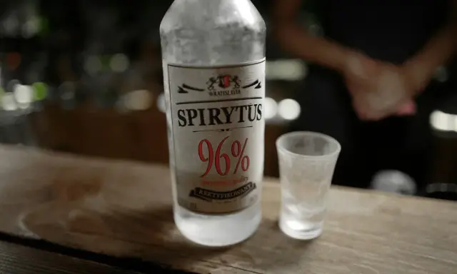 Spirytus 96% – alkohol, który ma najwięcej procent. Butelka i kieliszek na drewnianym blacie.