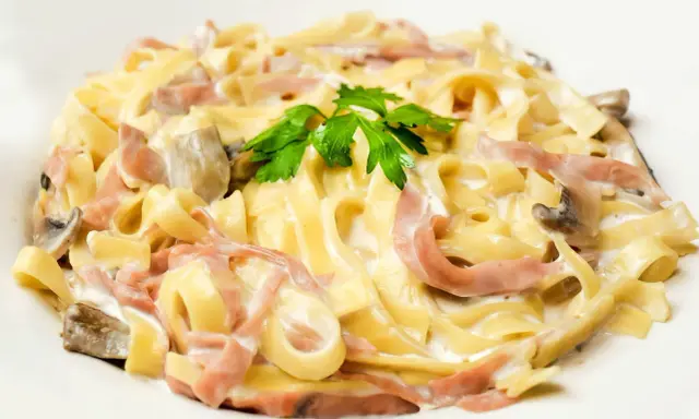 Tagliatelle z szynką i pieczarkami w kremowym sosie, ozdobione natką pietruszki. Pyszny makaron z mozzarellą w roli głównej.