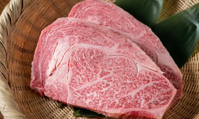 Dos cortes de carne japonesa cara, con marmoleado intenso, reposan sobre hojas verdes en una cesta de mimbre.