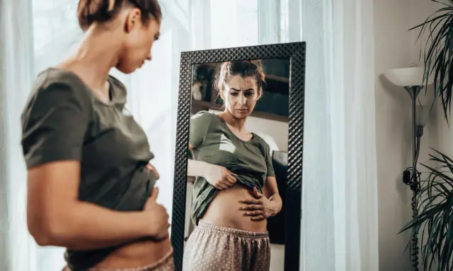 Kobieta zmartwiona dotyka brzucha, zastanawiając się, czy przy menopauzie boli brzuch.
