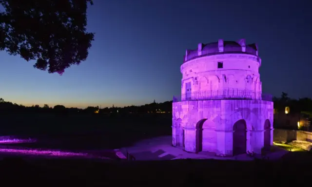 Torre antica illuminata di viola in una magica pink night. L'erba e gli alberi riflettono la luce, creando un'atmosfera surreale.