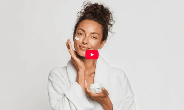 Donna sorridente applica crema viso, un gesto di skincare semplice per una pelle radiosa.