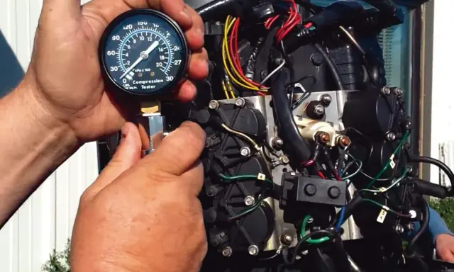 Mains d'un mécanicien utilisant un testeur de compression sur un moteur hors-bord. Le moteur se lance mais ne démarre pas essence.