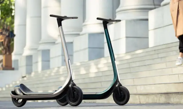 Deux trottinettes électriques modernes, idéales pour votre application trajet trottinette. L'une argentée, l'autre vert émeraude, sur des marches devant des colonnes.