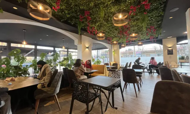 Intérieur d'un bar à desserts avec plafond végétalisée, lumières suspendues et tables occupées.