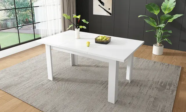Ett modernt, utdragbart vita matbord med en vas med gröna blad och en skål med äpplen.