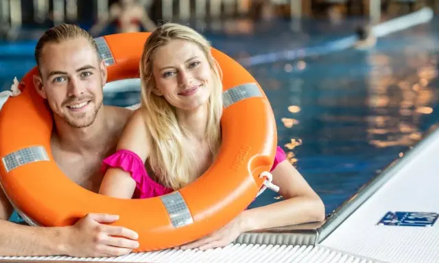 Uśmiechnięta para w basenie, trzymająca koło ratunkowe. Idealny weekend z przyjaciółką, pełen relaksu i zabawy w wodzie.