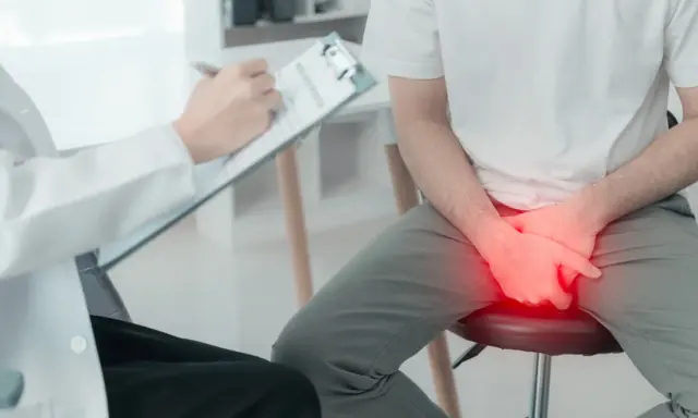 Lekarz spisuje zalecenia po cystoskopii. Pacjent siedzi, trzymając ręce na kroczu, gdzie widoczny jest czerwony obszar bólu.