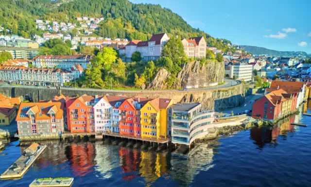 Kolorowe domy nad wodą w Bergen, idealne na norwegia zwiedzanie. W tle wzgórza porośnięte drzewami.
