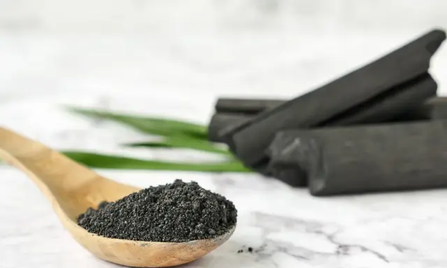 Drewniana łyżka z proszkiem, który może pomóc przy grypie. W tle węgiel aktywny w kawałkach.