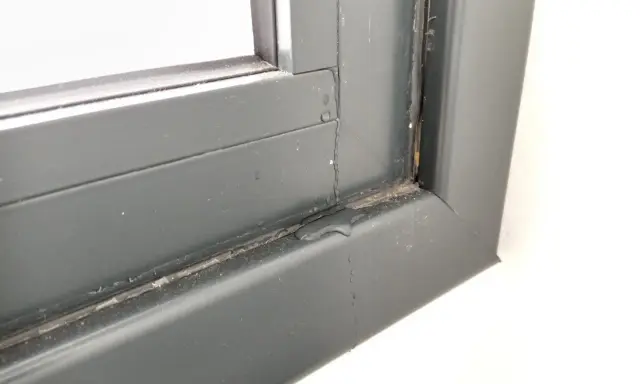 Gotas de lluvia resbalan por el marco de una ventana gris, dejando un rastro húmedo.