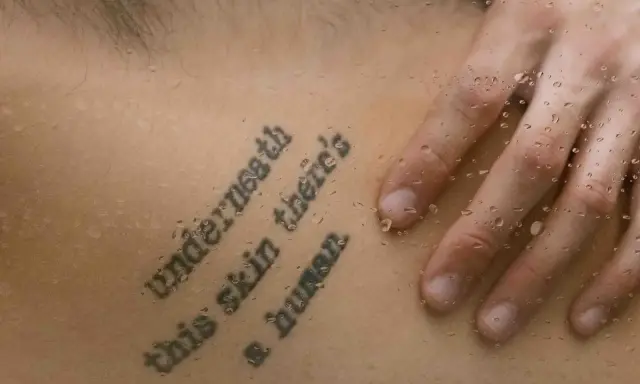 Tatuaż z cytatem "Underneath this skin there's a human" na skórze, z kroplami wody.