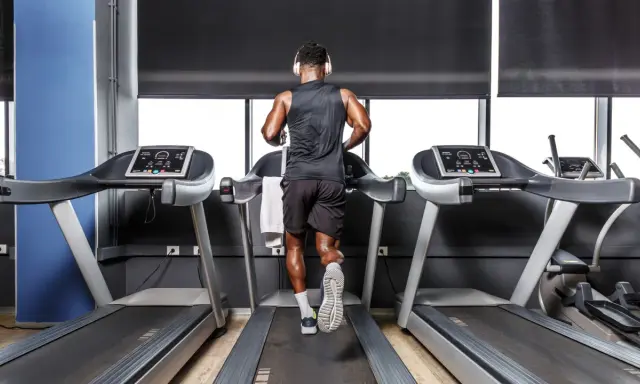 Mann mit Kopfhörern absolviert ein intensives Laufband Training in einem modernen Fitnessstudio.