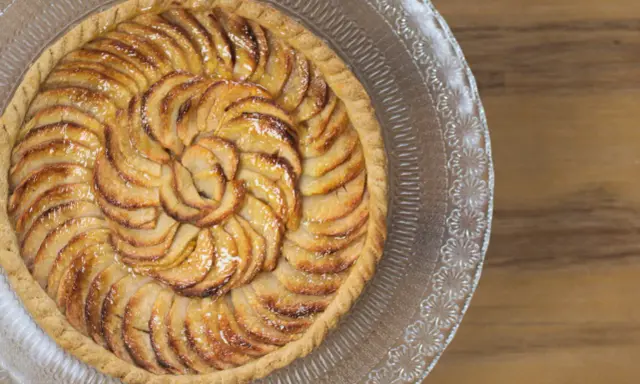 Tarte aux pommes dorée sur pâte feuilletée, disposée en spirale sur un plat en verre gravé. Un délice croustillant.