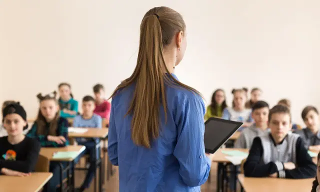 Lehrerin mit Tablet vor Schülern. Die Frage "wie viel verdient ein lehrer" beschäftigt viele.