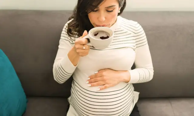 Schwangere Frau trinkt eine Tasse entkoffeinierten Kaffee, während sie ihren Bauch streichelt.