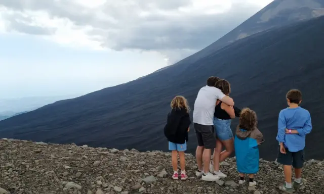 Famiglia in vacanza in Sicilia con bambini, ammira il pendio scuro di un vulcano.