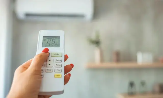 Mano con control remoto de aire acondicionado, ajustando el modo dry para dormir. La pantalla muestra 25°C.