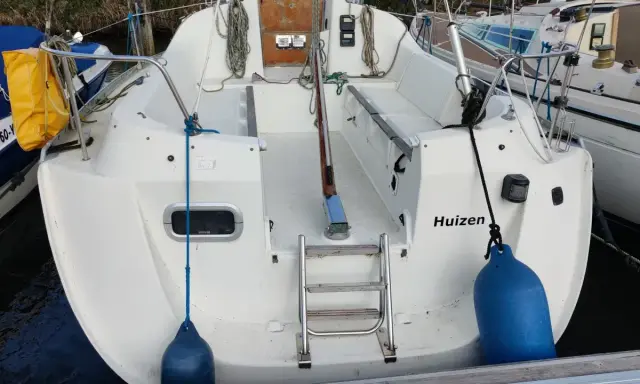 Vue arrière d'un voilier blanc amarré, avec le nom "Huizen" écrit sur la coque. Une échelle de bain est visible, ainsi que des pare-battages bleus. Le premier des 265 avis est prêt à être lu.