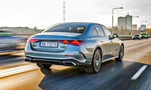 Elegancki, błękitny Mercedes E220d 4MATIC pędzi autostradą, mijając miejską panoramę.