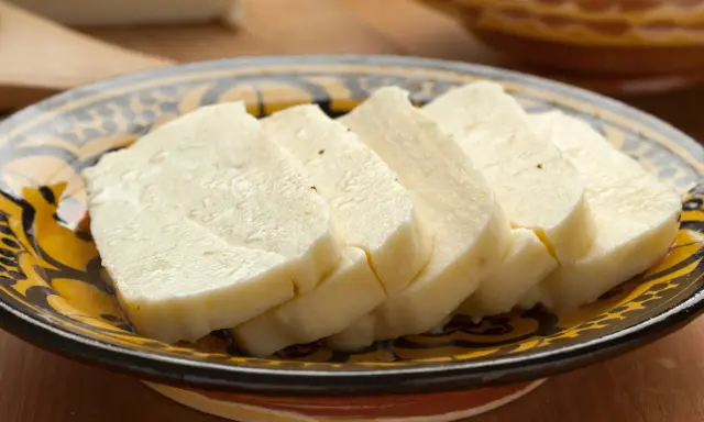 Pokrojony w plastry domowy ser halloumi na ozdobnym talerzu.