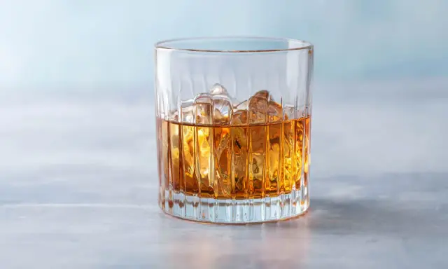 Ein Glas mit bernsteinfarbenem Getränk und Eiswürfeln, das an einen French Connection Cocktail erinnert.