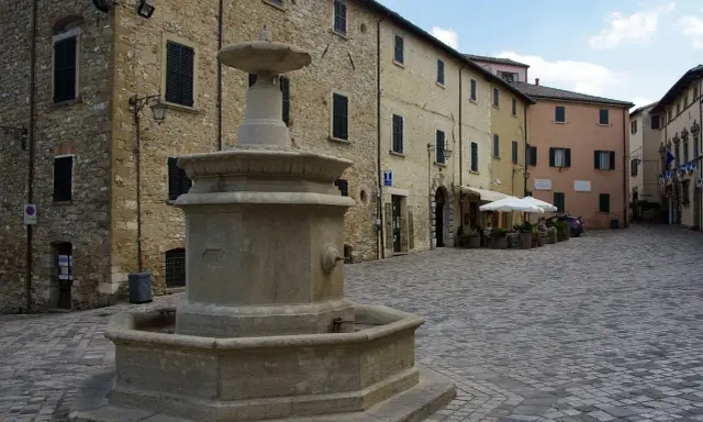 Piazza con fontana in pietra, circondata da edifici storici. Un angolo di pace nei borghi vicino Cattolica.