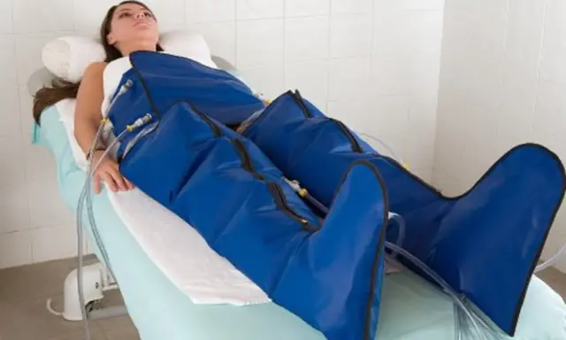 Kobieta leżąca na łóżku poddana zabiegowi presoterapii nóg w niebieskich mankietach.