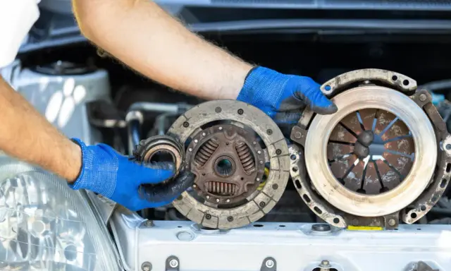 Mechanik w niebieskich rękawiczkach pokazuje zużyte części sprzęgła. Zastanawiasz się, ile kosztuje wymiana sprzęgła?