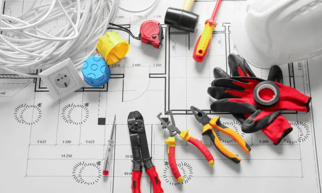 Outils d'électricien et rouleau de fil sur un plan architectural. Ce plan electrique maison détaille l'installation.