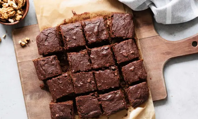 Brownies au chocolat coupés en carrés sur une planche en bois, accompagnés de noix. Un délicieux dessert healthy.