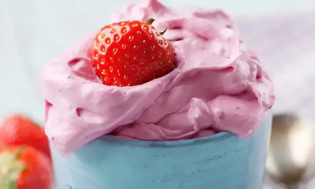Puszysty, różowy krem z mascarpone z truskawką na wierzchu, podany w niebieskim naczyniu.