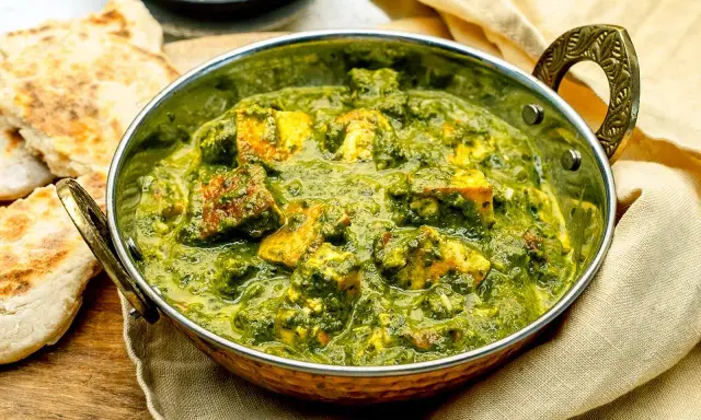 Ein köstliches Palak Paneer in einer traditionellen Schüssel, serviert mit Fladenbrot und Gewürzen.