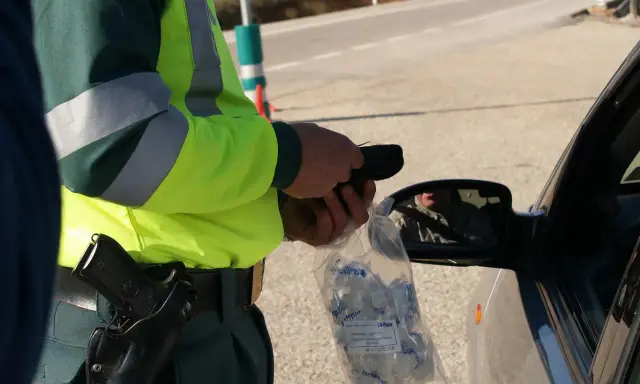 Policjant w kamizelce odblaskowej trzyma alkomat i worek z ustnikami przy samochodzie.