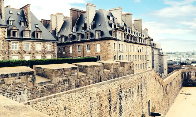 Murs de pierre de la ville fortifiée de Saint-Malo, avec des maisons bretonnes typiques et une vue sur la mer. Imaginez une pause à la taverne de Saint-Malo.