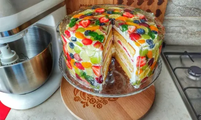 Kolorowy tort z owocami w żelu, z kawałkiem wyciętym, prezentuje się apetycznie.