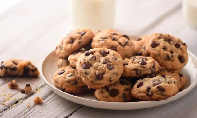 Une assiette de délicieux cookie fait maison, parsemés de pépites de chocolat, avec un verre de lait en arrière-plan.