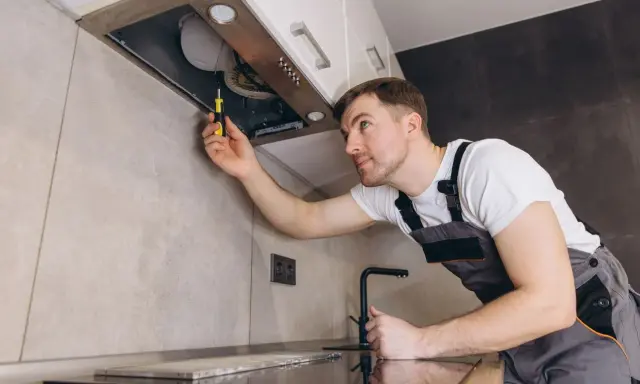 Un homme en salopette utilise un tournevis pour comment installer une hotte de cuisine.