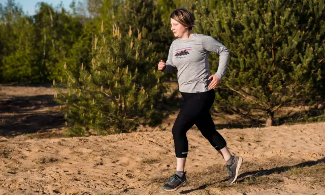 Frau beim **trail running** auf sandigem Untergrund, umgeben von Kiefern und Bäumen.