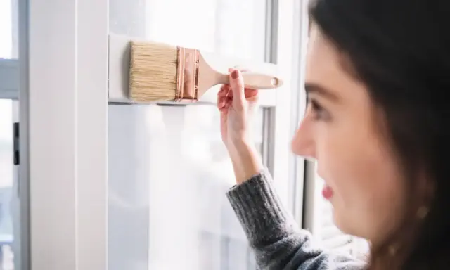 Mujer pintando un marco blanco de PVC con brocha. Aprende como pintar PVC para renovar tus espacios.
