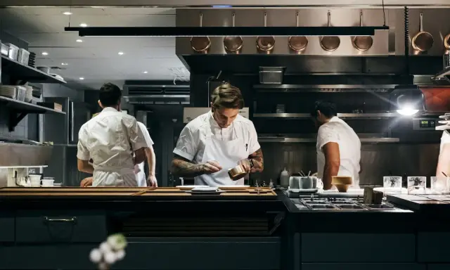 Chefs in a professional kitchen, one plating food.
