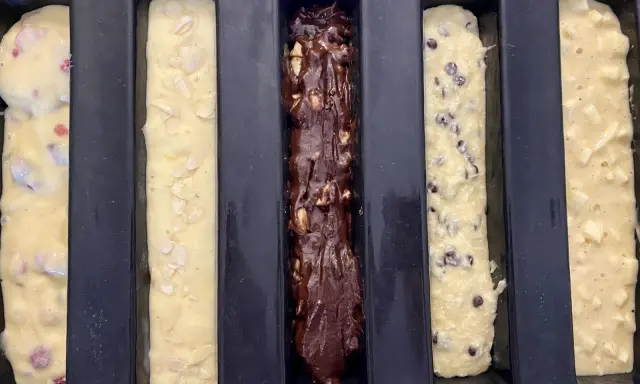 Cinq moules à cake longs prêts pour la cuisson : un aux fruits rouges, un aux amandes, un au chocolat, un aux pépites de chocolat et un aux pommes. Recette 5 cakes longs sucrés.