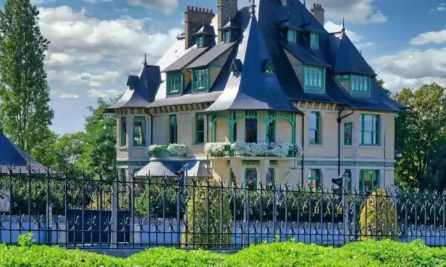 La villa Demoiselle à Reims, une demeure d'exception avec ses toits bleus et ses ornements verts, se dresse fièrement derrière une grille ouvragée.