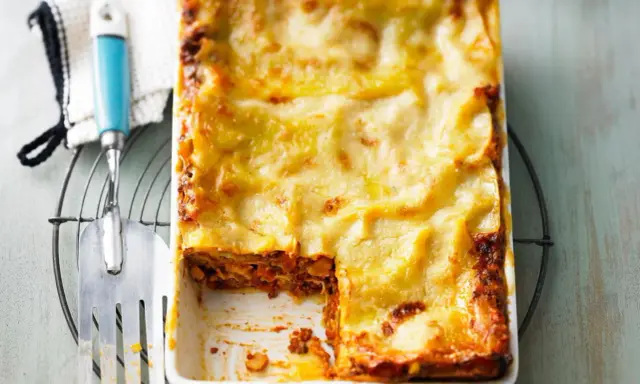 Eine frisch gebackene Lasagne al forno mit goldbraun überbackener Käseschicht, daneben ein Servierheber.