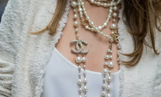 Eleganckie stylizacje z perłami, w tym wielowarstwowy naszyjnik Chanel z logo marki i perłami, dodają blasku białej bluzce i żakietowi.