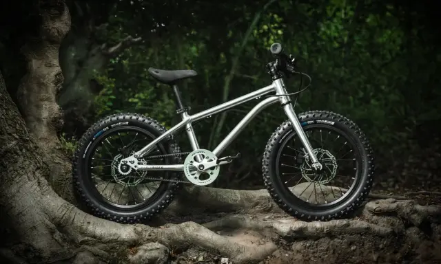 Srebrny rower dziecięcy z grubymi oponami, gotowy na wyzwania pumptracku. Jego lekka rama i solidne hamulce zapewnią bezpieczeństwo podczas pierwszych zjazdów.